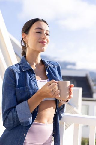 Young woman enjoying morning coffee on rooftop balcony with serene smile