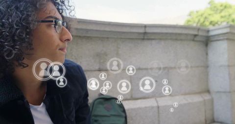 Young Man with Glasses Observing Virtual Network Icons Outdoors