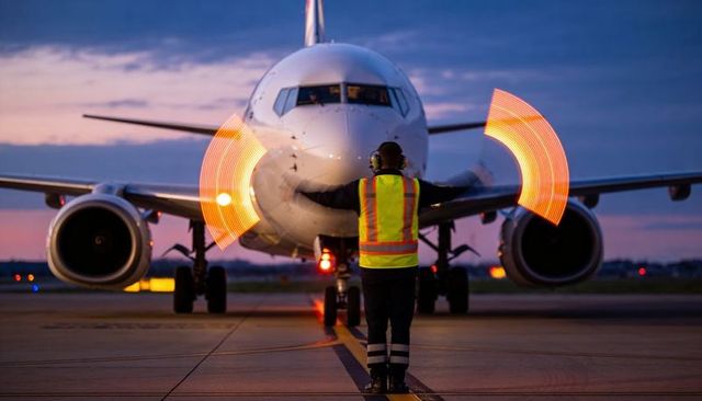 Ground marshaller waving illuminated wands guiding commercial jet on twilight ramp