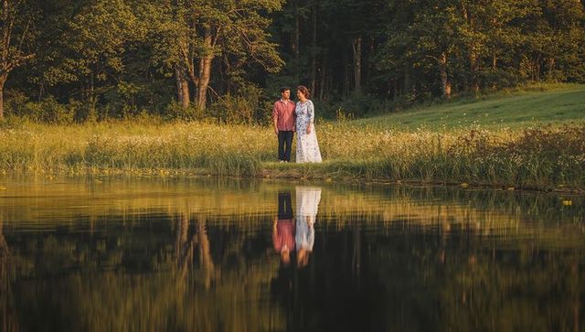 Lakeshore couple holding hands in red plaid shirt and floral dress, golden-hour reflection