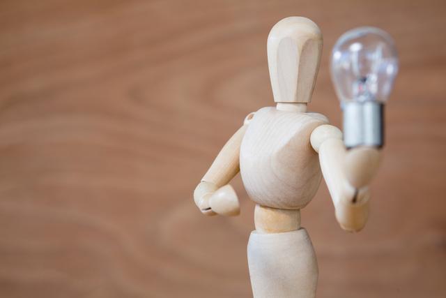 Wooden mannequin holding a light bulb symbolizing creativity, innovation, and bright ideas. Useful for illustrating concepts related to brainstorming, problem solving, and new ideas. Ideal for use in educational materials, business presentations, and creative projects.