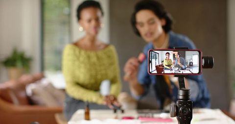 Asian man and african american woman filming at-home makeup tutorial on smartphone gimbal