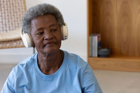 Senior african woman wearing headphones listening at home, relaxing in minimalist living room