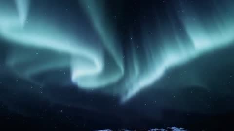 Timelapse swirling aurora borealis curling across starry sky above snow-covered ridge