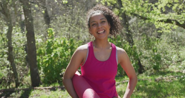 Cheerful woman smiling and stretching while enjoying an outdoor exercise session in a sunny forest. Perfect for promoting healthy lifestyles, fitness routines, outdoor activities, and wellness blogs.