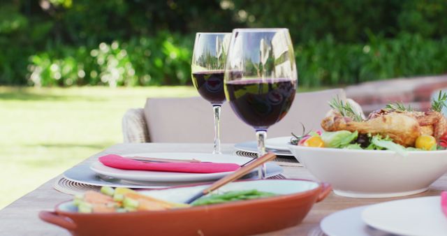 Close up of glasses of red wine and food on table in garden. Spending quality time with family at home concept.