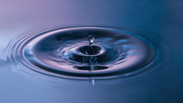 Single Water Droplet Rising Above Column Creating Ripples in Blue Violet Gradient