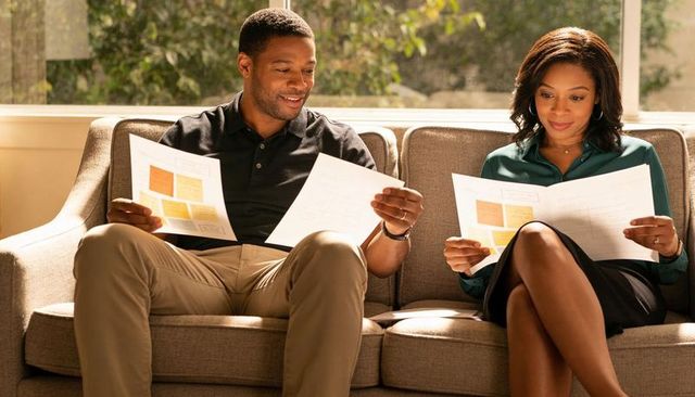 Couple reviewing financial paperwork on sunlit sofa, planning budget and home goals