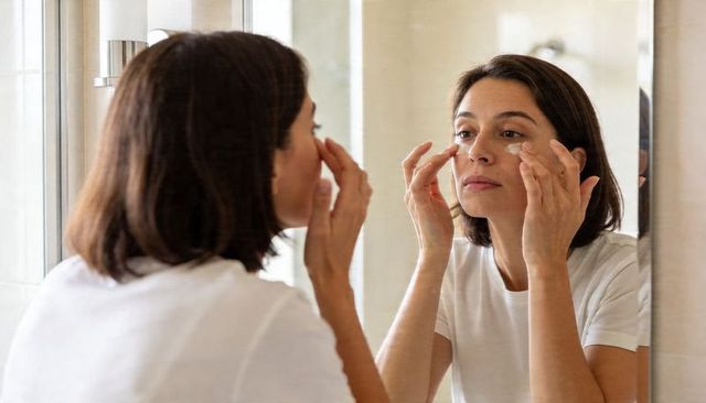 Woman applying hydrogel under-eye patches in minimalist bathroom mirror skincare routine