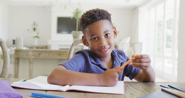 Young boy smiling while doing homework. Perfect for educational content, school-related advertisements, online tutoring service promotions, and articles about child education and learning at home.
