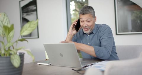 Senior man working remotely using smartphone and laptop at home