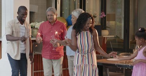 Multigenerational diverse family celebrating with sparklers on covered patio, outdoor party