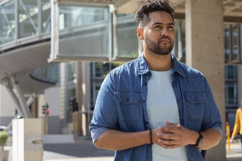 African man standing with hands clasped wearing denim shirt and smartwatch by glass walkway