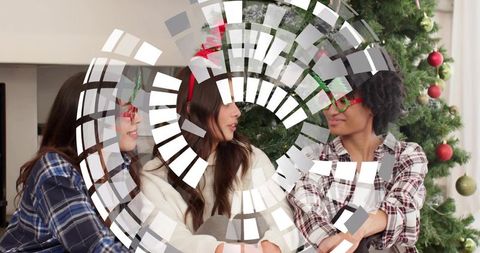 Three friends chatting beside christmas tree wearing festive glasses cozy holiday gathering