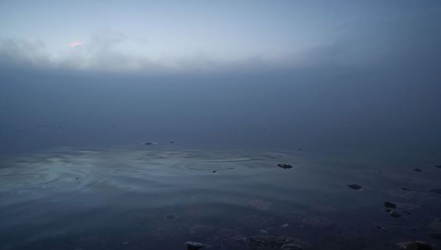 Misty twilight lake with glassy ripples, pebble shoreline and subtle pink glow