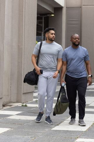 Two african american men walking after workout carrying duffel bags in urban sidewalk