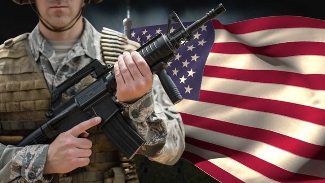 American soldier holding a rifle stands with a dynamic digital representation of the U.S. flag waving in the background. Ideal for illustrating themes of patriotism, military service, national pride, and American holidays. Useful in patriotic campaigns, military magazines, online articles, or veteran memorial promotions conveying strength and national pride.