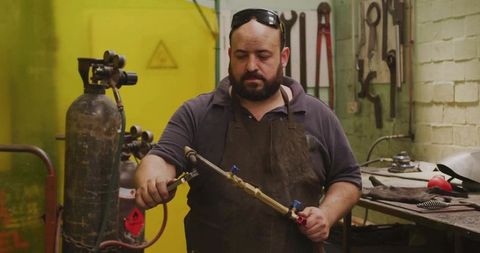 Bearded welder inspecting oxy-fuel torch valves in metal fabrication workshop