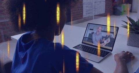 Clinician watching telemedicine consultation on laptop while wearing blue scrubs at desk