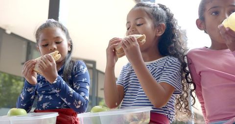 Three Young Girls Eating Lunch Together at School Table