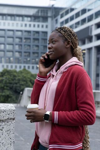 Young african american woman talking on phone holding coffee on city rooftop wearing smartwatch