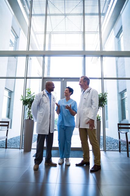 Medical team consisting of two doctors and a nurse discussing in a hospital lobby. Ideal for use in healthcare-related articles, medical team collaboration concepts, hospital brochures, and professional healthcare presentations.