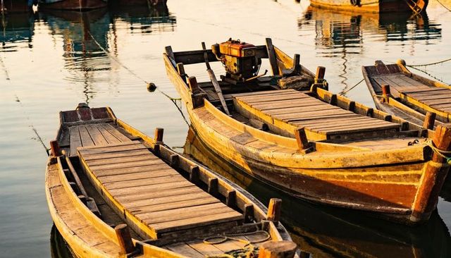 Sunlit wooden skiffs resting in tranquil harbor at dusk showing weathered plank decks, outboard moto