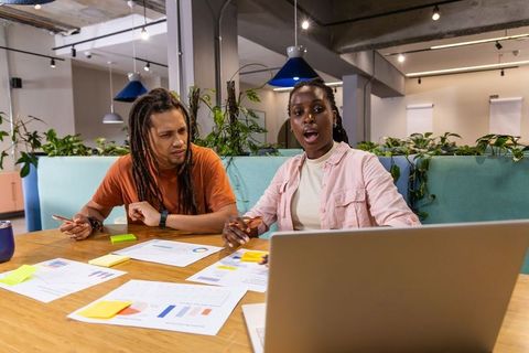 Diverse coworkers brainstorming over charts and laptop in modern vibrant coworking space
