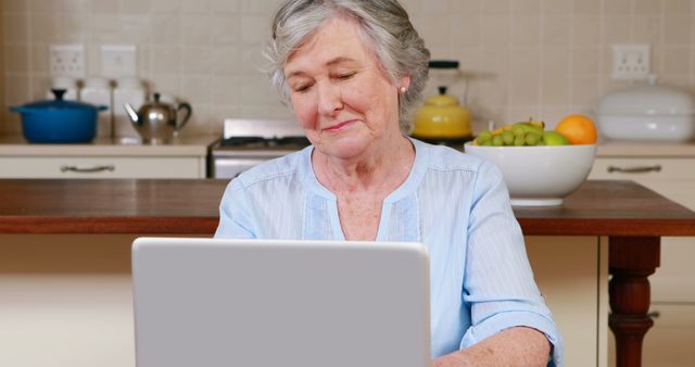 Elderly woman engaging with laptop in kitchen for online activity or communication - Download Free Stock Images Pikwizard.com