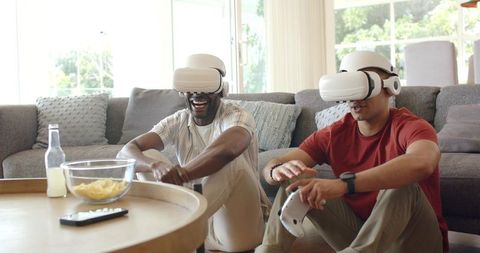 Diverse male friends enjoying VR gaming at home sitting on floor with controllers and snacks