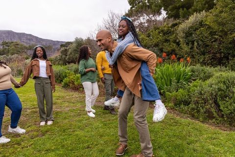 African american family laughing and playing outdoors with father giving daughter piggyback