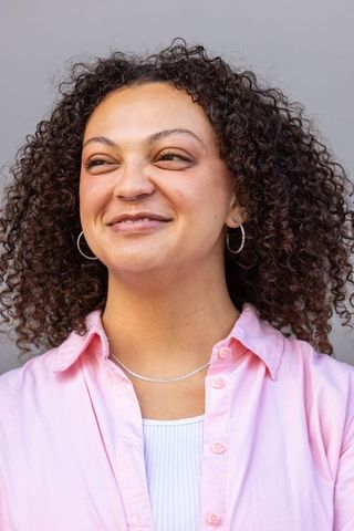 Confident african american woman smiling, looking right, curly hair headshot in pink shirt