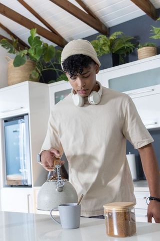 African american man pouring hot water into mug during calm morning routine in modern kitchen