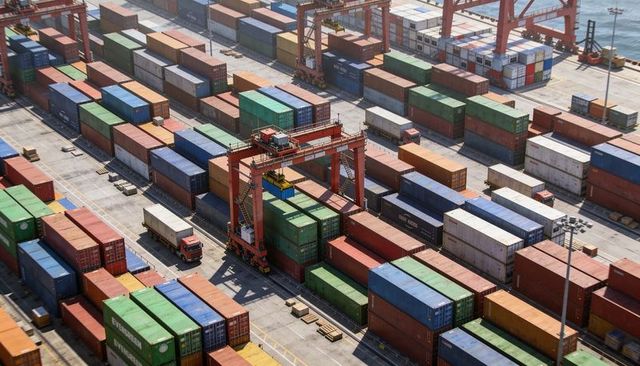 Gantry crane lifting shipping container over colorful stacked containers, aerial port
