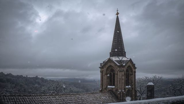 Snow-capped gothic church spire overlooking misty valley with golden finial