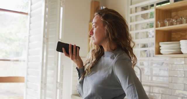 Business professional is talking on a smartphone while standing near a window flooded with sunlight. Ideal for concepts related to remote work, communication, modern office settings, and technology usage. Useful for illustrating articles, advertisements, and presentations about business, professional communication, and lifestyle themes.