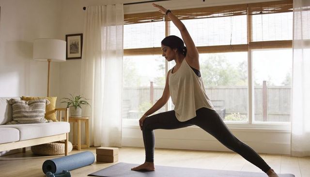 Woman practicing lunge yoga in bright minimalist living room with natural wood accents and yoga prop