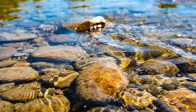 Sunlit riverbed with glistening submerged stone, ripples, bubbles and golden reflections