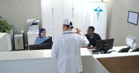 Clinician gesturing at clinic reception desk with staff coordinating patient care