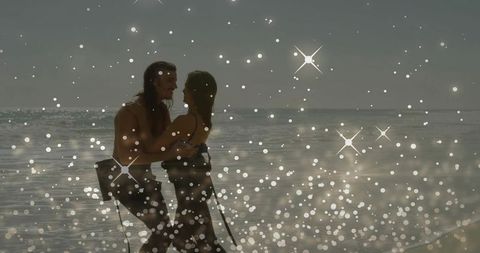 Sunlit romantic embrace on shoreline with sparkling bokeh silhouette at golden hour