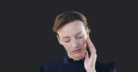 Contemplative woman touching cheek wearing ruffled navy blouse minimal studio portrait