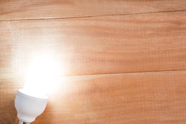 This image shows a close-up of a glowing bulb placed on a wooden surface. The bright light contrasts with the natural wood texture, creating a warm and inviting atmosphere. Ideal for use in articles or advertisements related to home decor, interior design, energy efficiency, or modern living spaces.