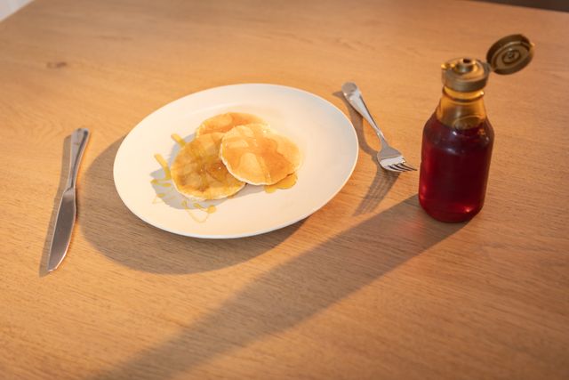 Three pancakes on a plate and a maple syrup bottle next to it. Food and breakfast. 