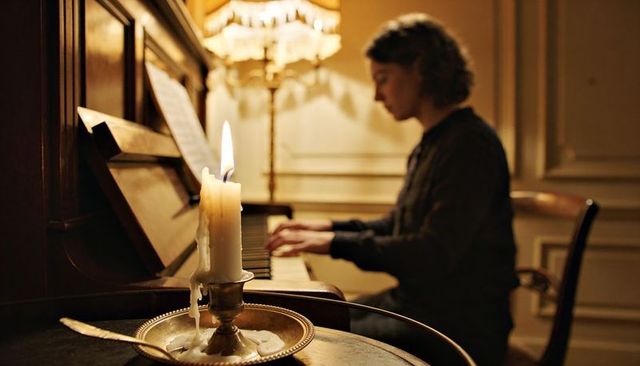 Candlelit pianist playing vintage upright piano in elegant parlor