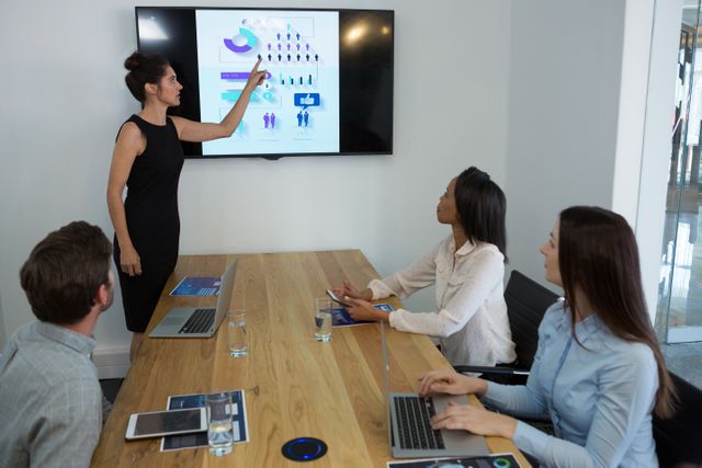Female executive giving a presentation to her colleagues in a modern conference room. Ideal for use in business, corporate training, teamwork, leadership, and professional development contexts.