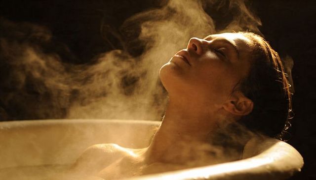 Steamy bathtub portrait: woman reclining with closed eyes in warm golden light