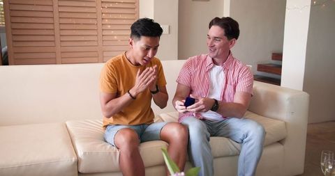 Joyful Diverse Male Couple Sharing Smile While Watching Smartphone