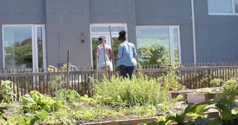African woman and youth tending raised urban garden beds in front of modern gray building