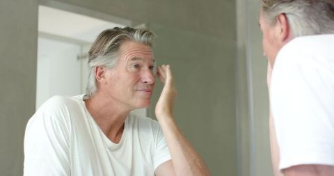 Mature man applying skincare at bathroom mirror, morning grooming and self care routine