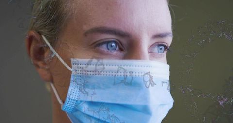 Mature woman wearing surgical mask gazing with expressive blue eyes and stud earring